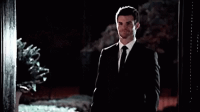 A Man In A Suit And Tie Is Standing In Front Of A Doorway . GIF