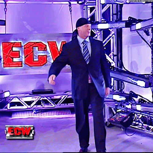 A Man In A Suit And Tie Is Standing In Front Of A Ecw Logo GIF