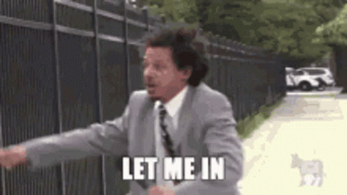 A Man In A Suit And Tie Is Standing In Front Of A Fence And Says `` Let Me In '' . GIF