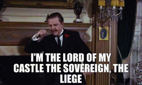 A Man In A Suit And Tie Is Standing In Front Of A Fireplace And Talking On A Phone . GIF