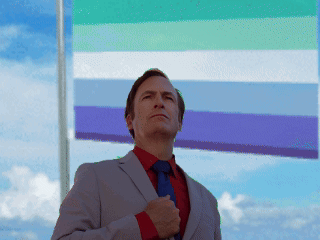 A Man In A Suit And Tie Is Standing In Front Of A Flag GIF