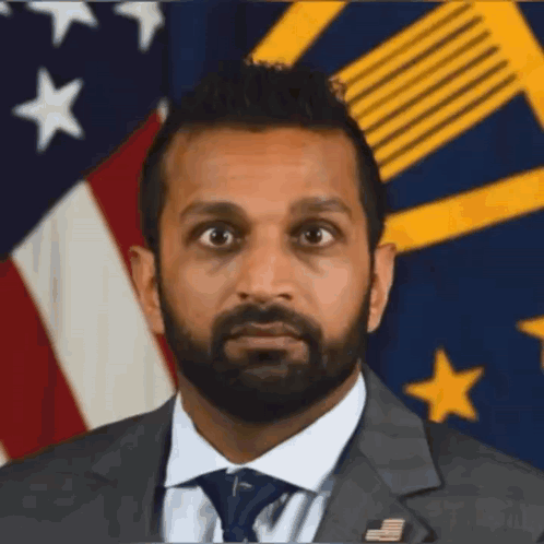 A Man In A Suit And Tie Is Standing In Front Of A Flag GIF