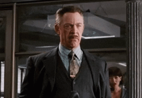 A Man In A Suit And Tie Is Standing In Front Of A Glass Door GIF