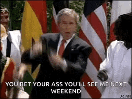 A Man In A Suit And Tie Is Standing In Front Of A Group Of Flags . GIF