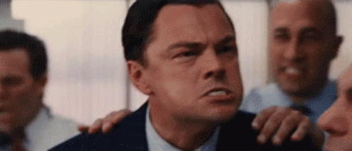 A Man In A Suit And Tie Is Standing In Front Of A Group Of Men And Making A Funny Face . GIF