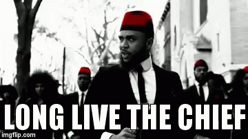 A Man In A Suit And Tie Is Standing In Front Of A Group Of Men Wearing Red Hats And Ties . GIF