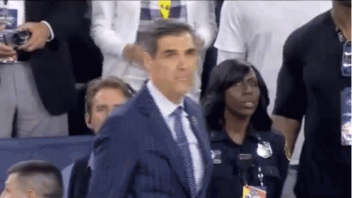 A Man In A Suit And Tie Is Standing In Front Of A Group Of People . GIF