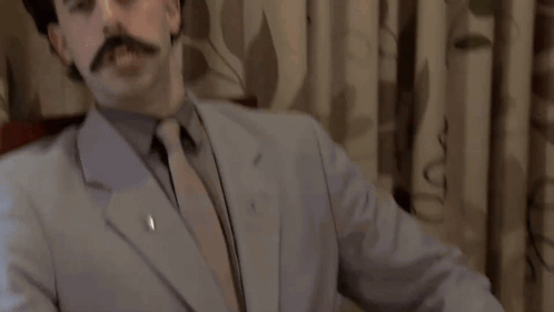 A Man In A Suit And Tie Is Standing In Front Of A King Sign GIF