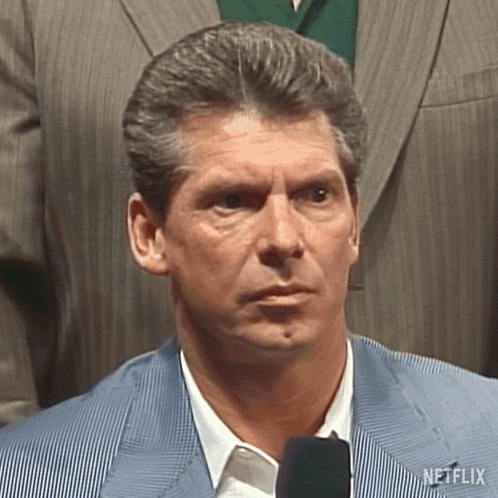 A Man In A Suit And Tie Is Standing In Front Of A Microphone And Looking At The Camera . GIF