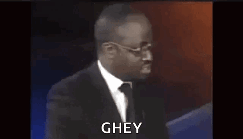 A Man In A Suit And Tie Is Standing In Front Of A Microphone And Says Ghey . GIF