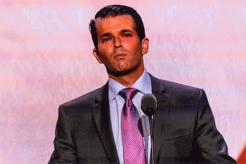 A Man In A Suit And Tie Is Standing In Front Of A Microphone GIF