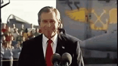 A Man In A Suit And Tie Is Standing In Front Of A Microphone . GIF
