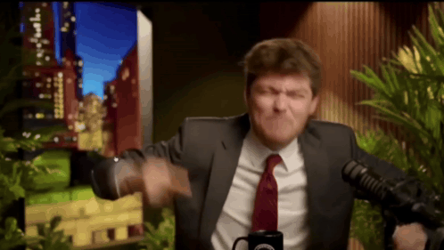 A Man In A Suit And Tie Is Standing In Front Of A Microphone With A Mug In Front Of Him That Says Cbs GIF