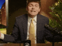 A Man In A Suit And Tie Is Standing In Front Of A Microphone With His Arms Outstretched GIF