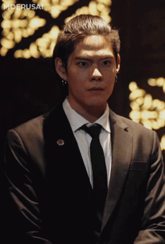 A Man In A Suit And Tie Is Standing In Front Of A Moerusai Logo GIF