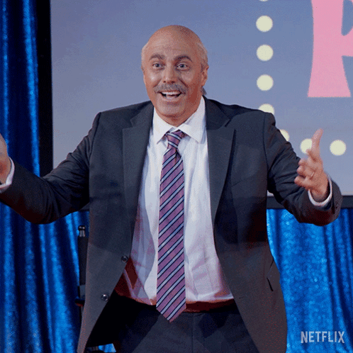 A Man In A Suit And Tie Is Standing In Front Of A Netflix Sign GIF