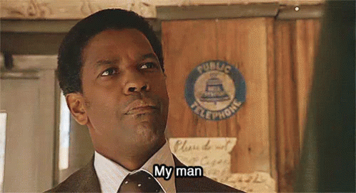 A Man In A Suit And Tie Is Standing In Front Of A Public Telephone Sign And Saying `` My Man '' . GIF