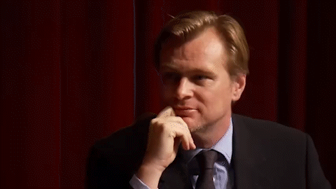A Man In A Suit And Tie Is Standing In Front Of A Red Curtain . GIF