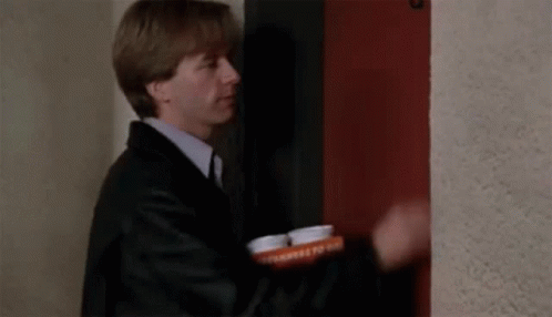 A Man In A Suit And Tie Is Standing In Front Of A Red Door Holding A Tray Of Pills . GIF
