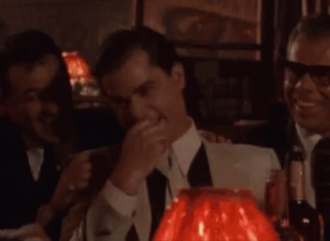 A Man In A Suit And Tie Is Standing In Front Of A Red Lamp In A Bar . GIF