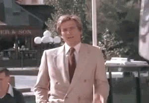 A Man In A Suit And Tie Is Standing In Front Of A Restaurant . GIF