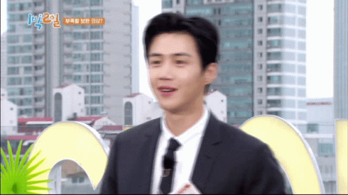 A Man In A Suit And Tie Is Standing In Front Of A Sign That Says 1 2 GIF