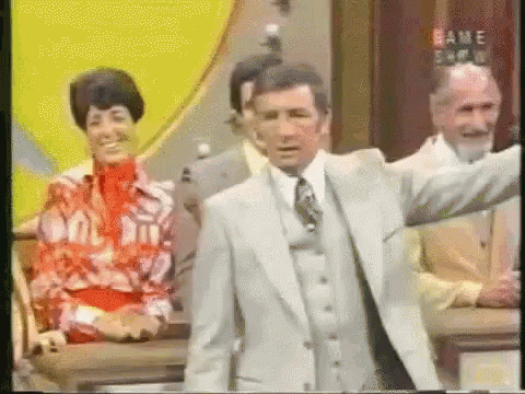 A Man In A Suit And Tie Is Standing In Front Of A Sign That Says " Game Show " GIF