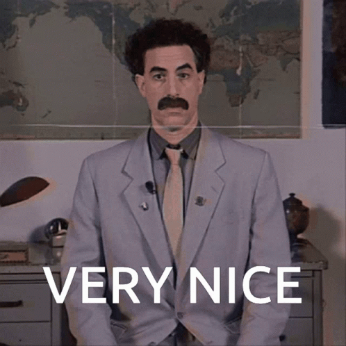 A Man In A Suit And Tie Is Standing In Front Of A Sign That Says " Very Nice " GIF