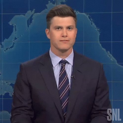 A Man In A Suit And Tie Is Standing In Front Of A Snl Sign GIF
