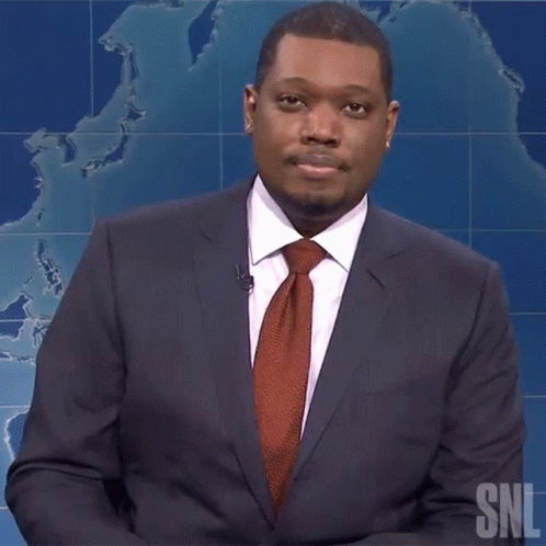 A Man In A Suit And Tie Is Standing In Front Of A Snl Sign GIF