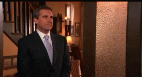 A Man In A Suit And Tie Is Standing In Front Of A Staircase GIF