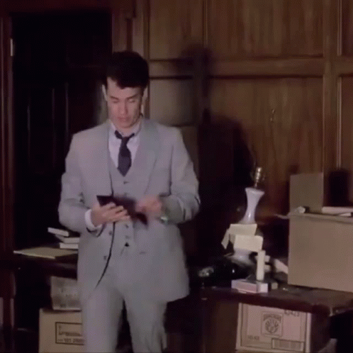 A Man In A Suit And Tie Is Standing In Front Of A Table With Boxes On It And A Lamp On Top GIF