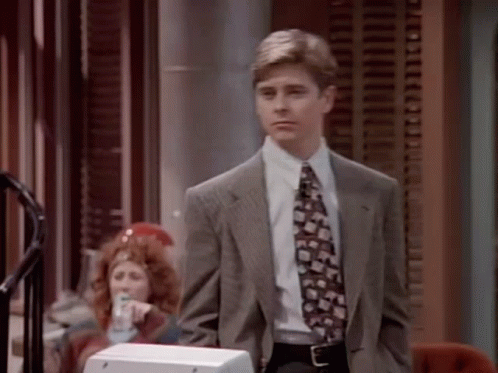 A Man In A Suit And Tie Is Standing In Front Of A Telephone GIF