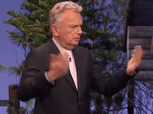 A Man In A Suit And Tie Is Standing In Front Of A Tree GIF
