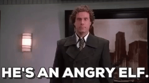 A Man In A Suit And Tie Is Standing In Front Of A Wall And Says `` He 'S An Angry Elf '' . GIF