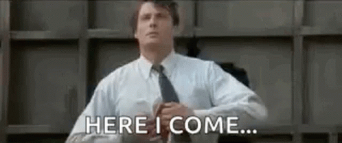 A Man In A Suit And Tie Is Standing In Front Of A Wall And Says `` Here I Come '' . GIF