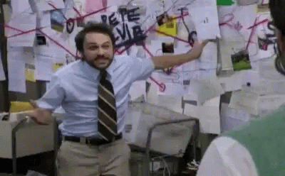 A Man In A Suit And Tie Is Standing In Front Of A Wall Covered In Posters . GIF