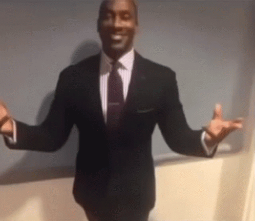 A Man In A Suit And Tie Is Standing In Front Of A Wall With His Arms Outstretched . GIF