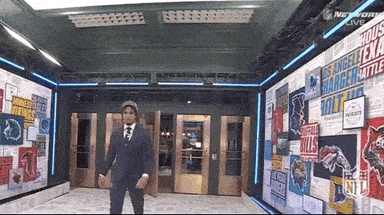 A Man In A Suit And Tie Is Standing In Front Of A Wall With Nfl Logos GIF