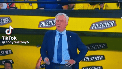 A Man In A Suit And Tie Is Standing In Front Of A Wall With Pilsener Advertisements GIF