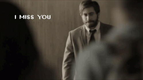 a man in a suit and tie is standing in front of a wall with the words i miss you above him