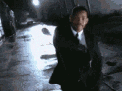 A Man In A Suit And Tie Is Standing In Front Of A White Car GIF
