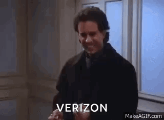 A Man In A Suit And Tie Is Standing In Front Of A Window And Holding A Verizon Phone . GIF