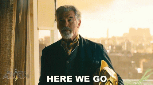 A Man In A Suit And Tie Is Standing In Front Of A Window And Says Here We Go GIF