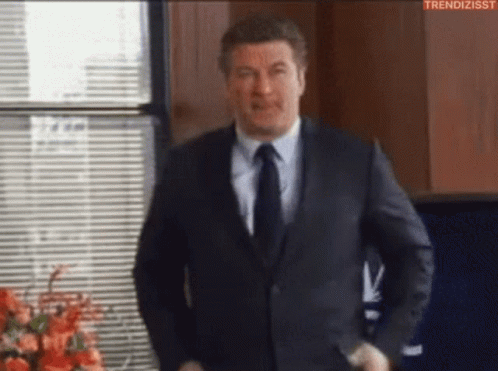 Man In Suit And Tie Standing In Front Of Window With Blinds GIF