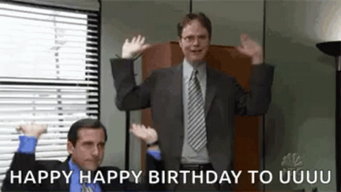 A Man In A Suit And Tie Is Standing In Front Of A Window With His Hands In The Air . GIF