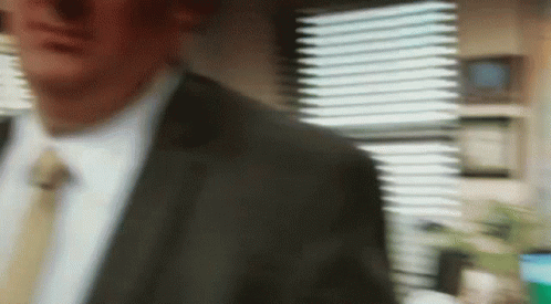 A Man In A Suit And Tie Is Standing In Front Of A Window GIF