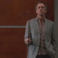 A Man In A Suit And Tie Is Standing In Front Of A Wooden Wall Holding A Cell Phone . GIF