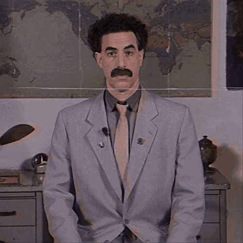 A Man In A Suit And Tie Is Standing In Front Of A World Map GIF