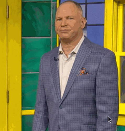 A Man In A Suit And Tie Is Standing In Front Of A Yellow Door And Window . GIF
